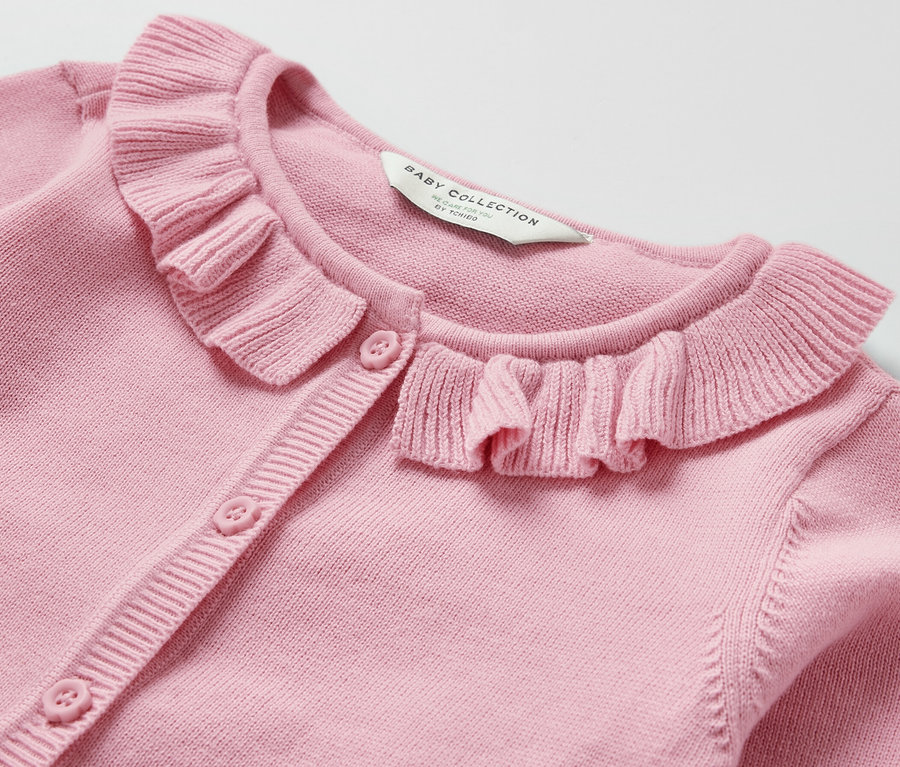 Gros plan d'une jaquette en maille pour bébé rose avec un col à volants et une fermeture boutonnée.