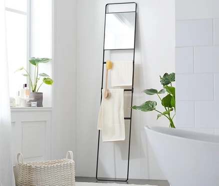 Échelle à serviettes noire avec miroir et deux serviettes dans la salle de bain.