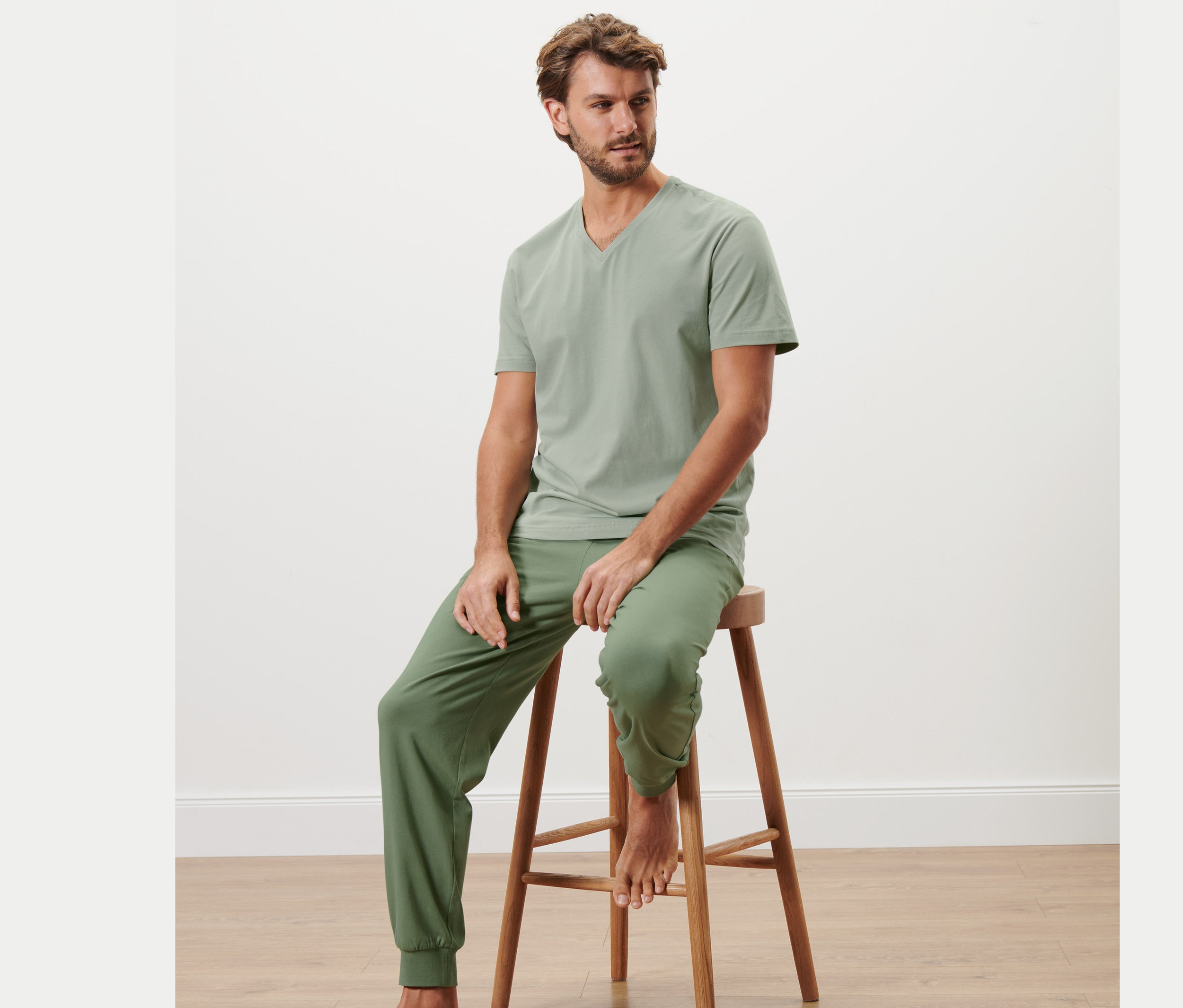 Un homme est assis sur un tabouret en bois et porte un pyjama.