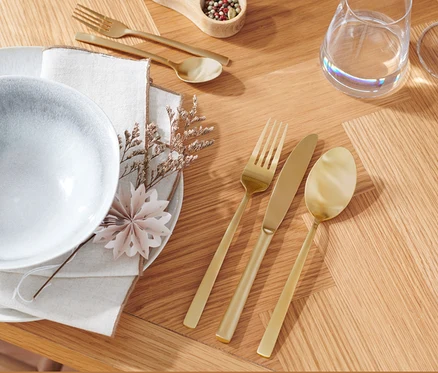 Assiette, serviette et ensemble de couverts de 20 pièces couleur or champagne sur une table en bois.