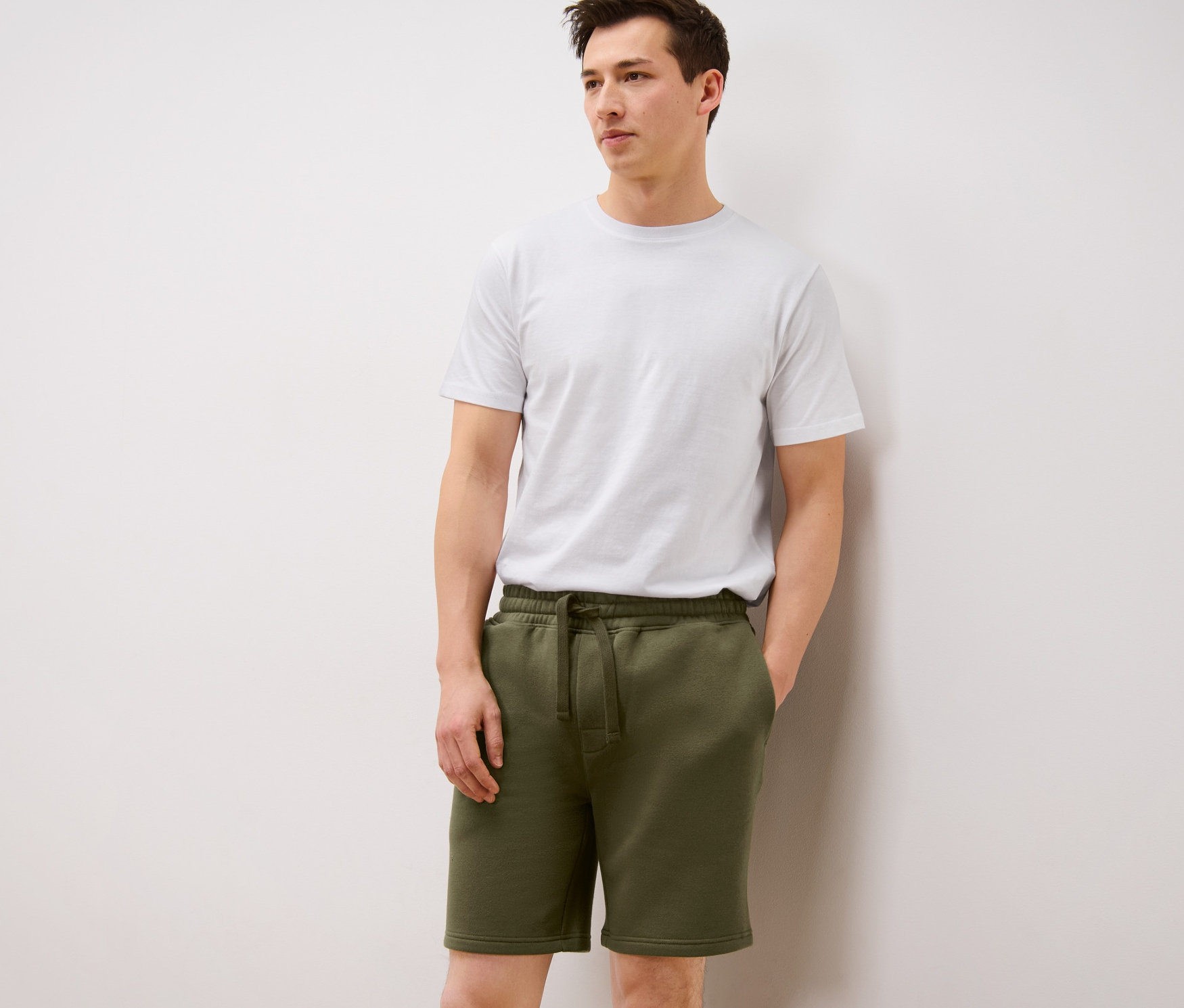 Un homme porte un short de survêtement olive et un t-shirt blanc.