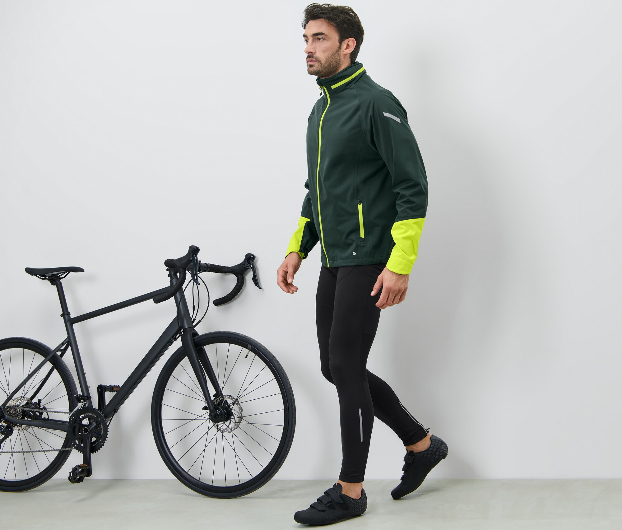 Un homme marche à côté d'un vélo noir et porte un cuissard de vélo.