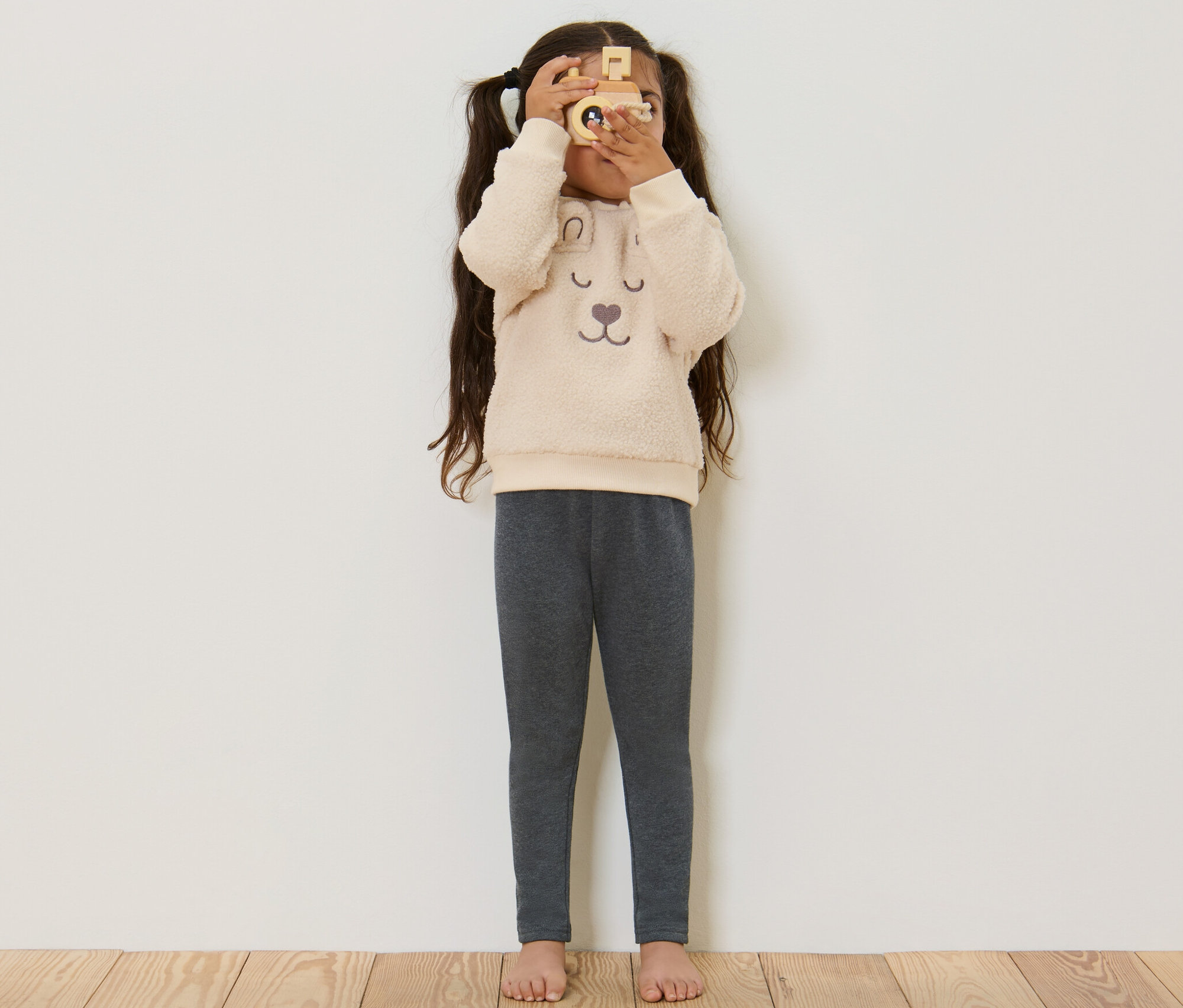 Fillette regardant à travers un appareil photo en bois et portant un legging thermique pour enfant gris.