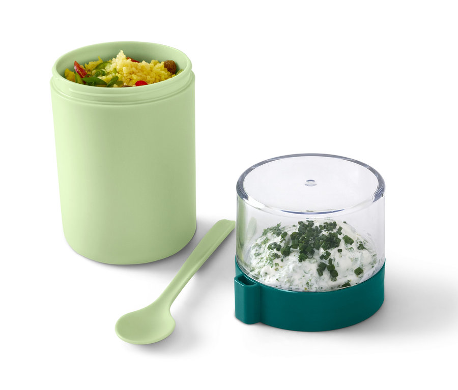 Un récipient de transport pour yaourt vert avec du contenu, à côté d'une cuillère et d'un récipient avec du fromage frais aux herbes.