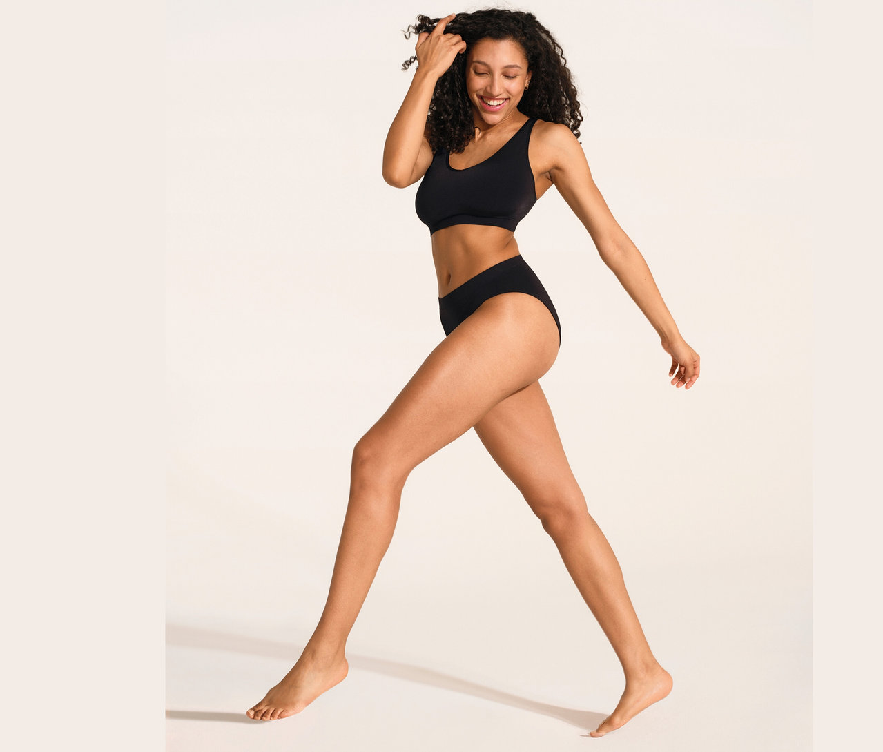 Une femme marche et sourit, elle porte une brassière douce SCHIESSER noire avec coussinets et un slip SCHIESSER Rio noir.