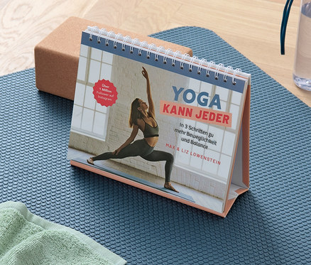 Un tapis de yoga bleu avec une serviette, un bloc et le livre « Yoga kann jeder ».