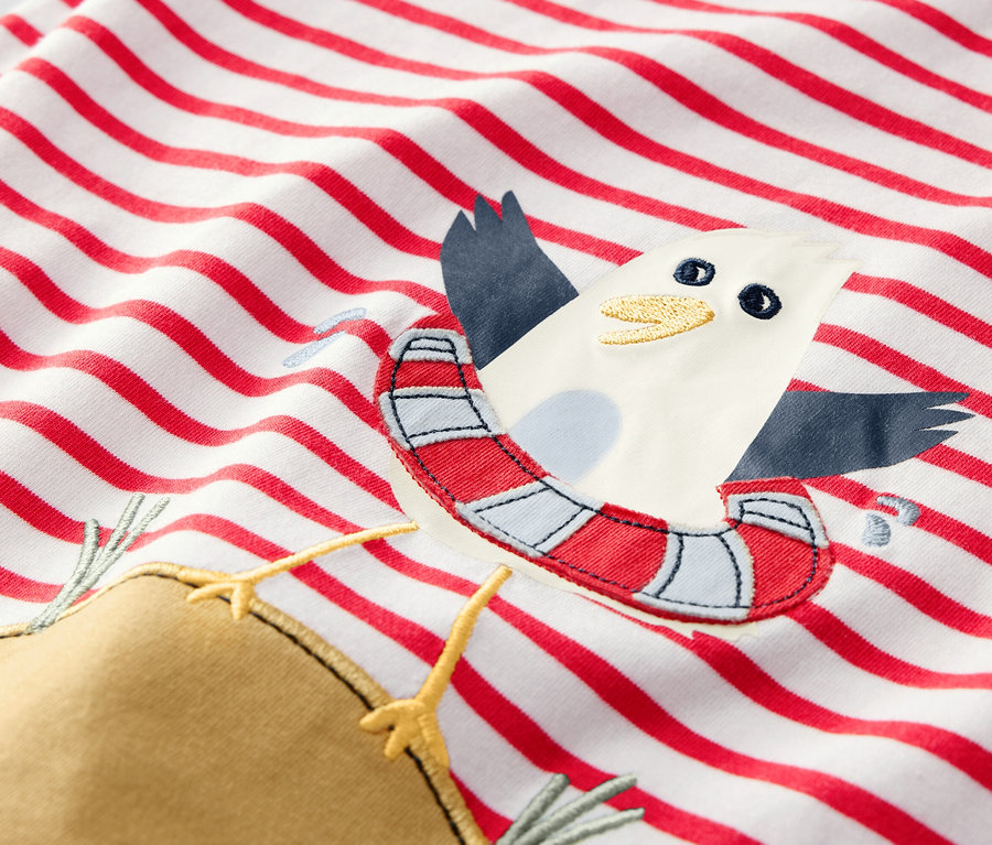 Détail d'un t-shirt pour enfant avec des rayures rouges et une application de mouette avec une bouée.