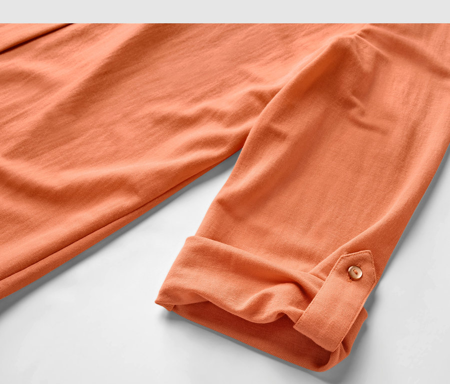 Gros plan sur un chemisier en jersey piqué pêche avec des manches retroussées.