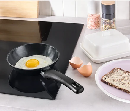 Sur une plaque de cuisson noire se trouve une mini-poêle avec revêtement anti-adhésif dans laquelle cuit un œuf au plat.