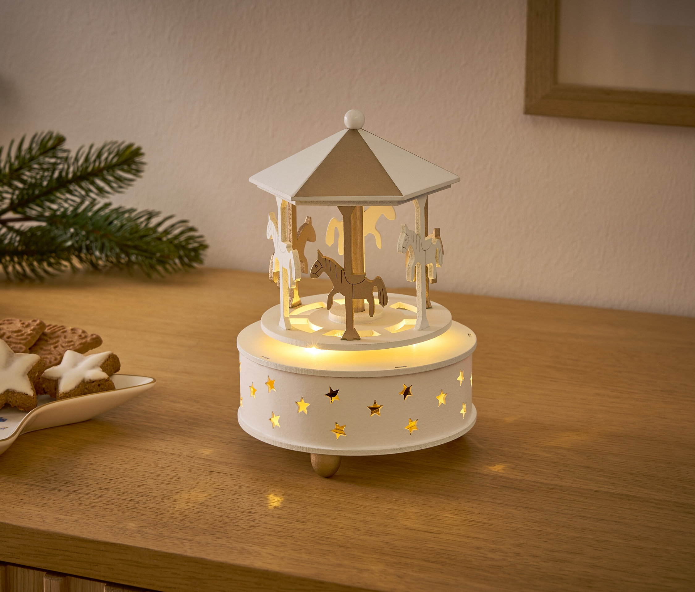 Un manège en bois avec des chevaux et des étoiles illumine une table en bois à côté des biscuits de Noël.