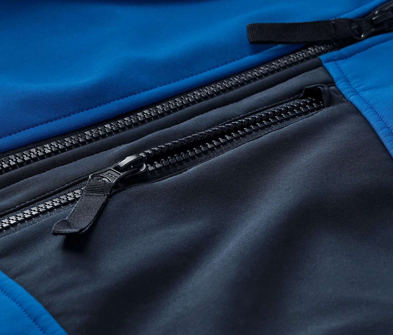 Détail d'une veste softshell bleu et noire avec des fermetures éclair.