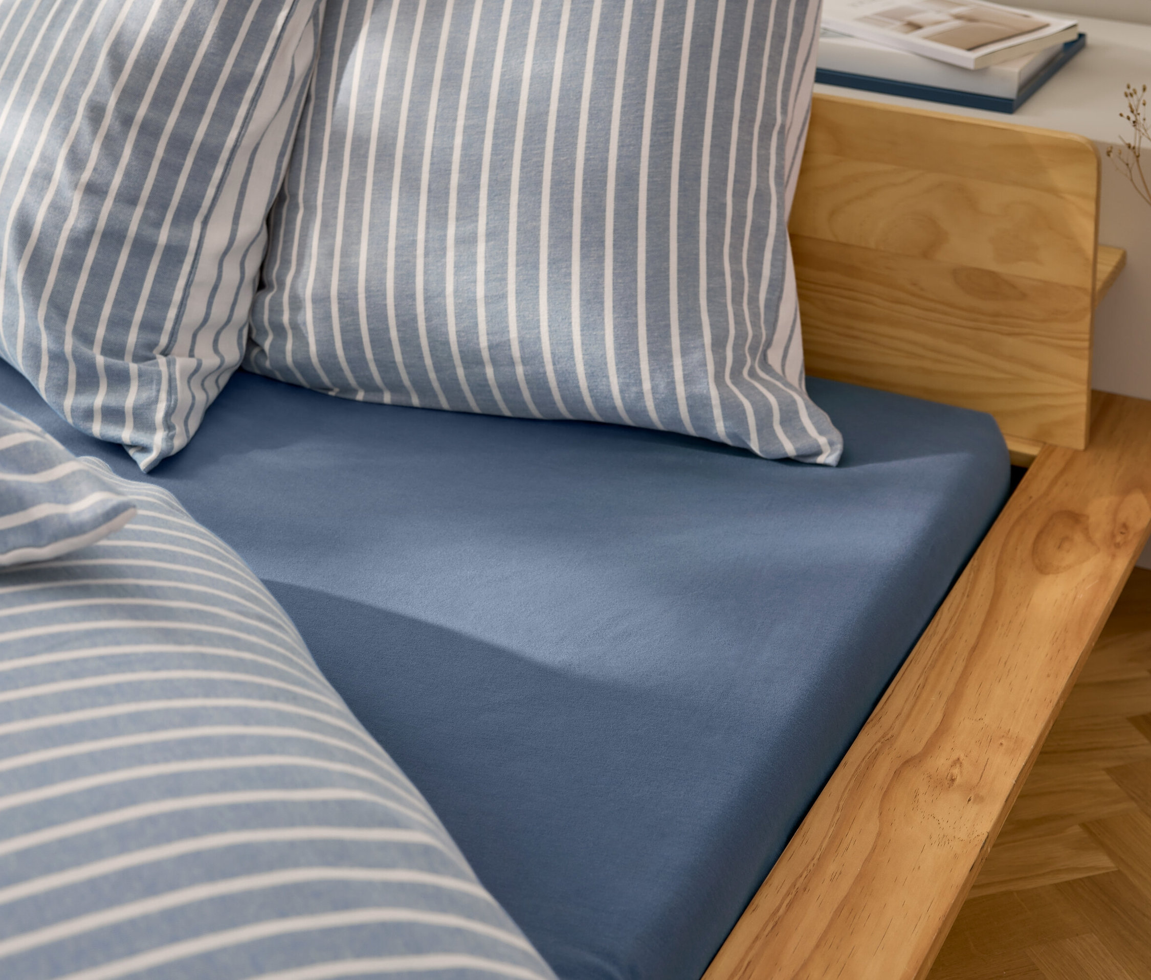 Drap-housse bleu sur lit en bois avec oreillers rayés.
