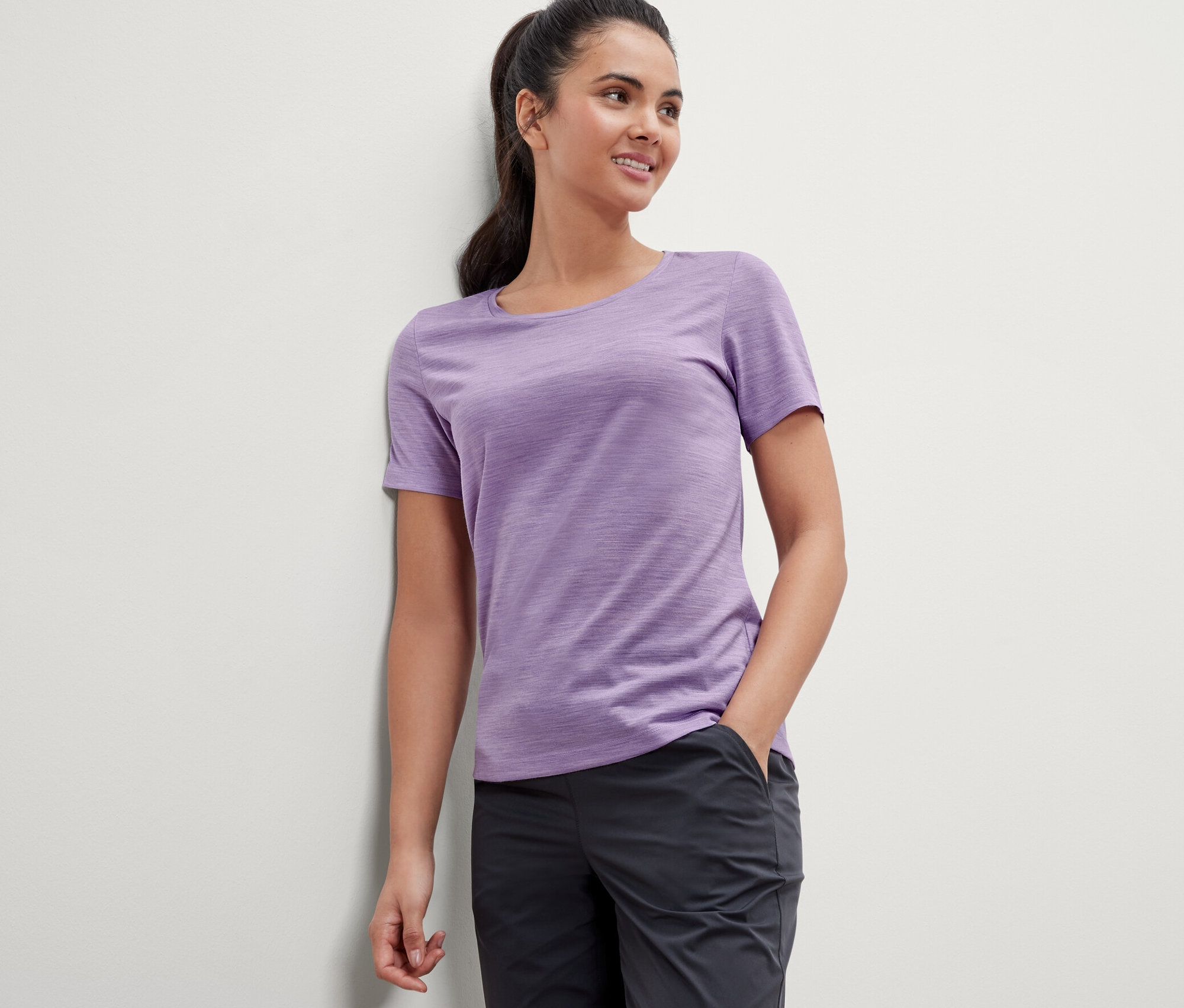 Une femme appuyée contre un mur porte un t-shirt violet en laine mérinos.