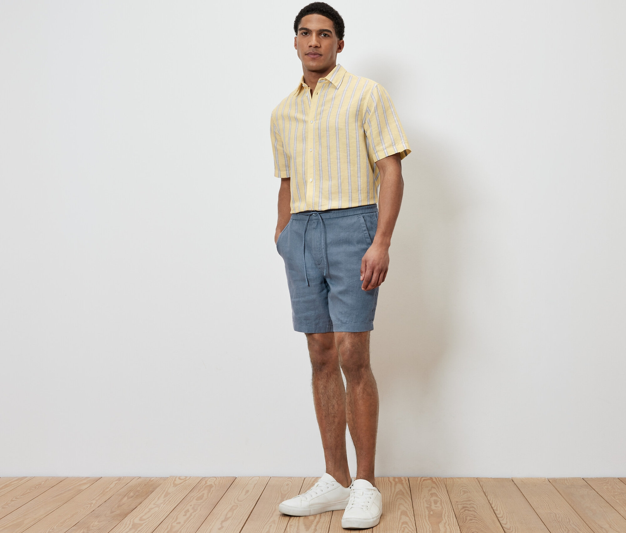 Un homme debout portant un short en lin bleu et une chemise jaune.