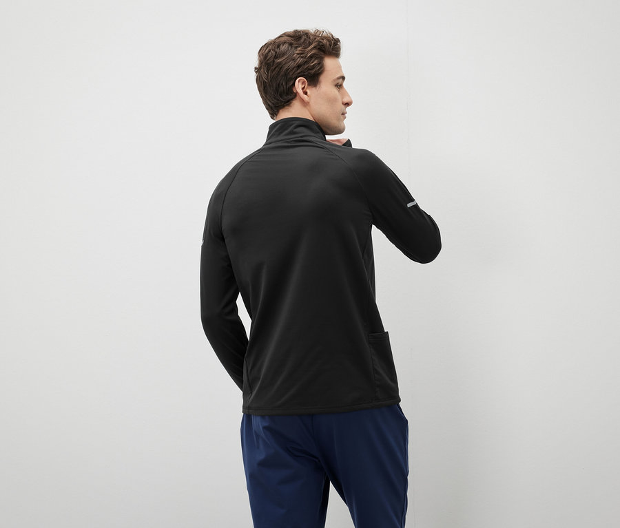 Un homme portant un pull noir zippé et un pantalon bleu, regardant vers la gauche.