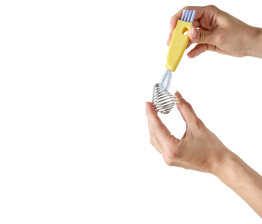 Des mains nettoient un fouet spirale avec une brosse jaune.