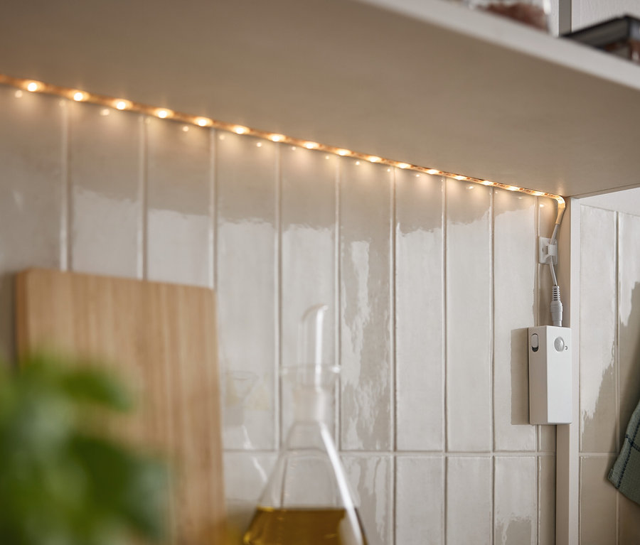 Une bande LED éclaire sous une armoire sur des carreaux blancs.