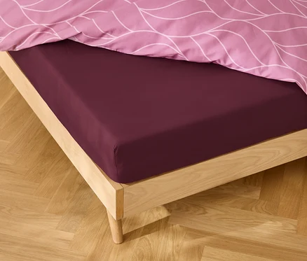 Gros plan d'un lit avec un drap-housse bordeaux et du linge de lit rose à motifs.