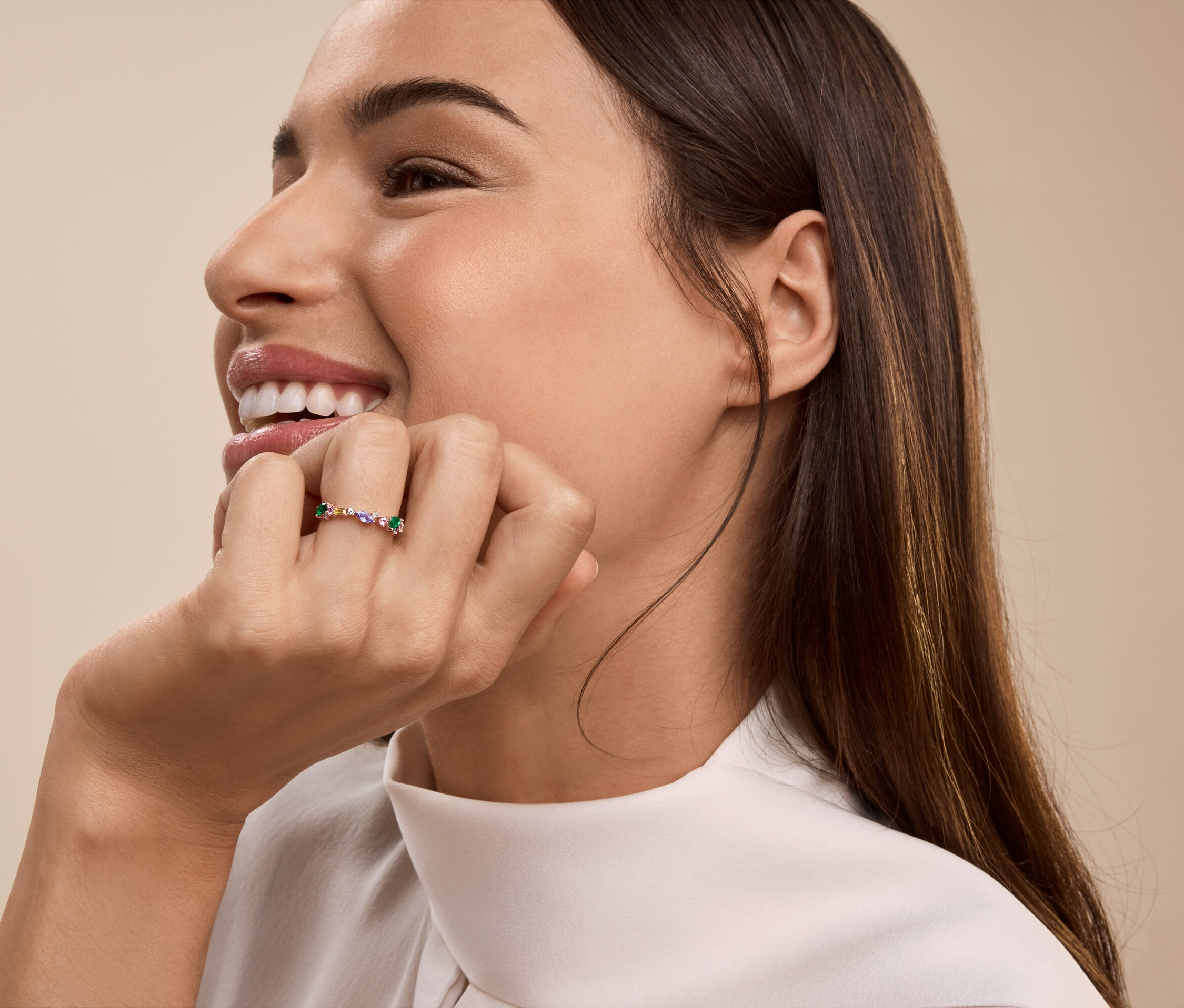Une femme sourit, sa main soutenant son menton, portant une bague à son doigt.
