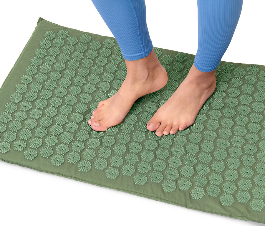 Les pieds d'une personne portant des leggings bleus se tiennent sur un tapis d'acupression vert.