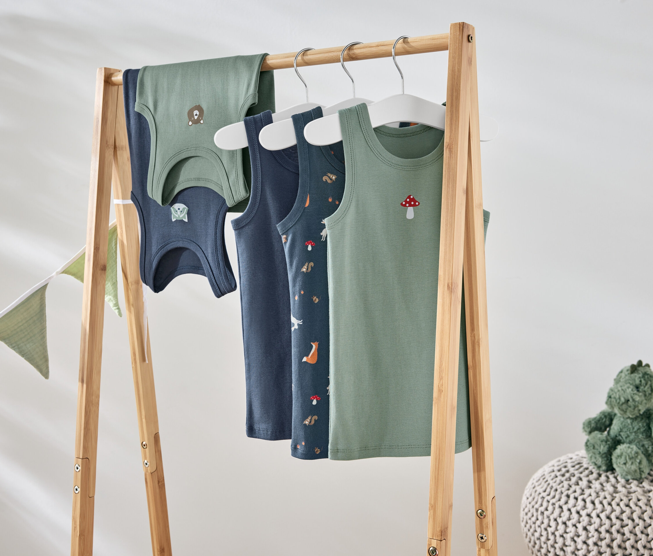 Quatre débardeurs avec différents motifs suspendus à un support en bois.