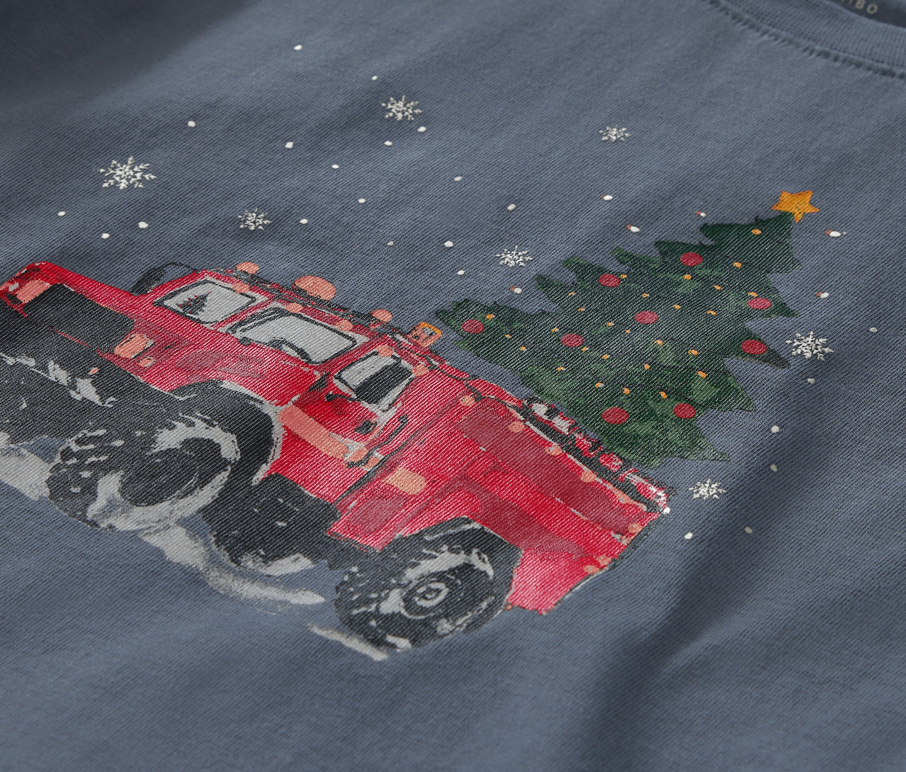 Gros plan d'un t-shirt bleu avec un imprimé représentant une voiture rouge à côté d'un arbre de Noël et de flocons de neige.