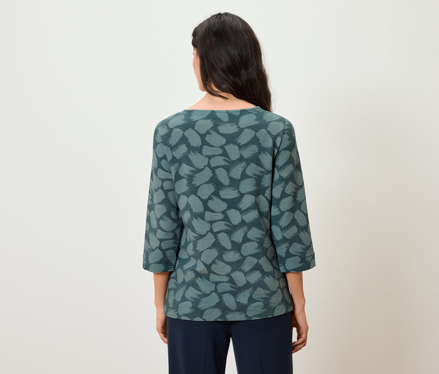 Vue arrière d'une femme aux longs cheveux foncés portant un haut bleu-vert à manches trois-quarts et un pantalon bleu foncé.