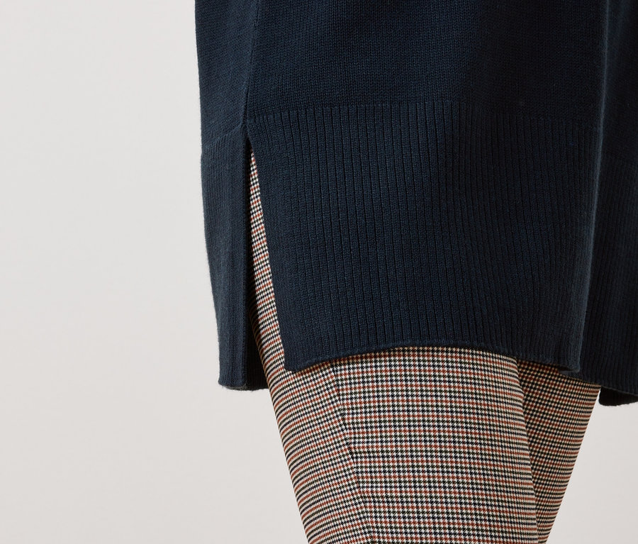 Détail d'une tenue féminine avec un pull bleu foncé fendu et un pantalon à carreaux.