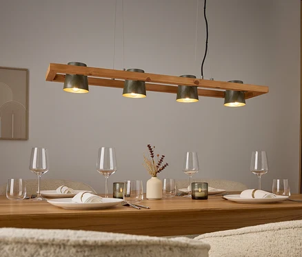 Quatre lampes grises au-dessus d'une table en bois avec des couverts et des verres.