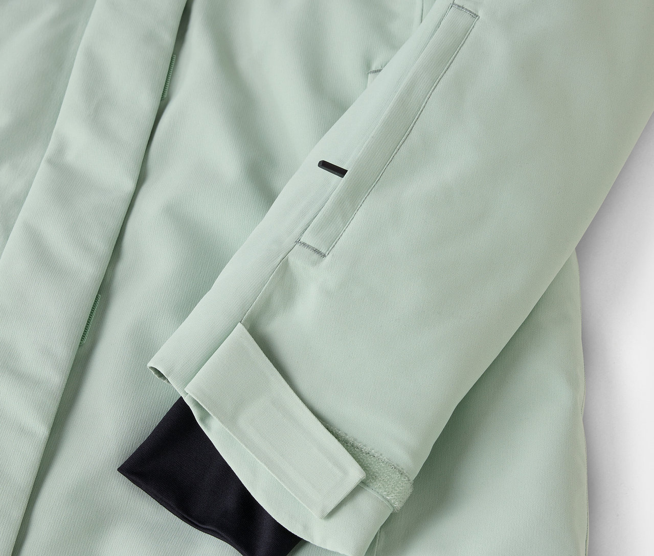 Détail d'une veste vert clair avec manchette noire et poche sur la manche.