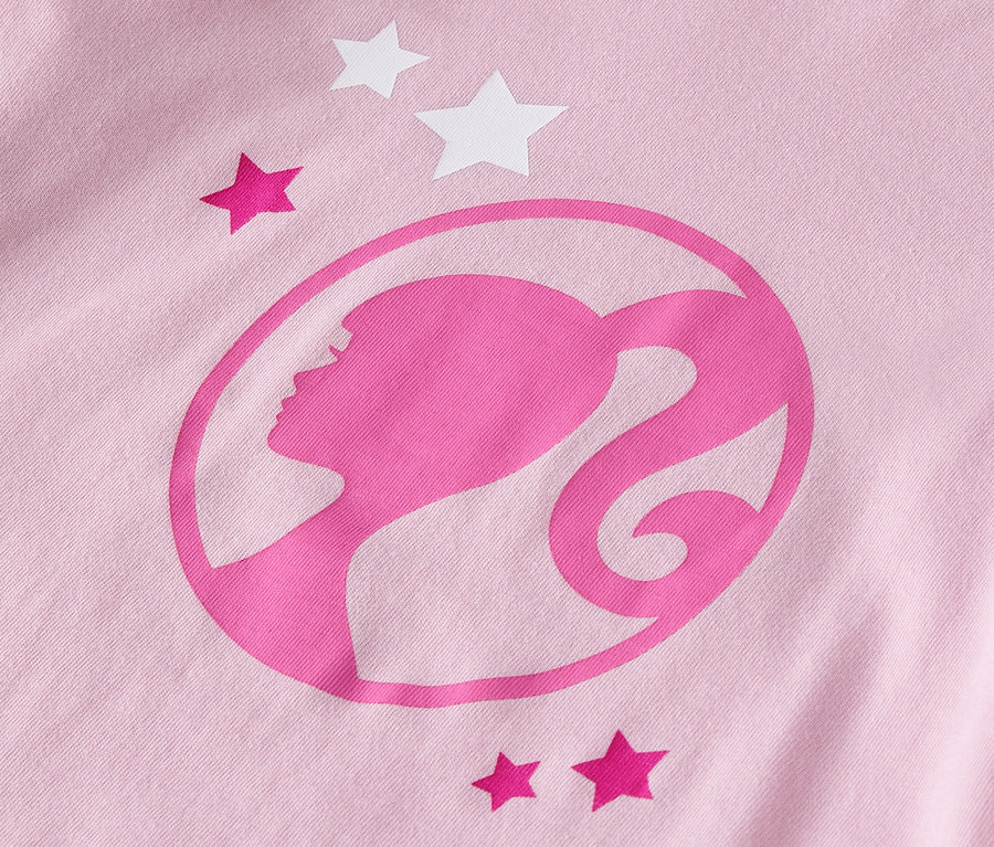 Gros plan sur un t-shirt rose avec le logo Barbie et des étoiles.