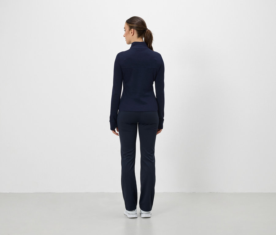 Une femme, dos à la caméra, porte une veste de sport et un pantalon bleu marine.