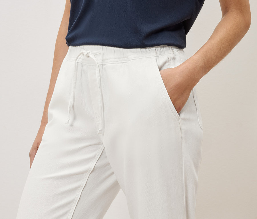 Une femme a la main dans la poche d'un pantalon blanc avec élastique et cordon de serrage.
