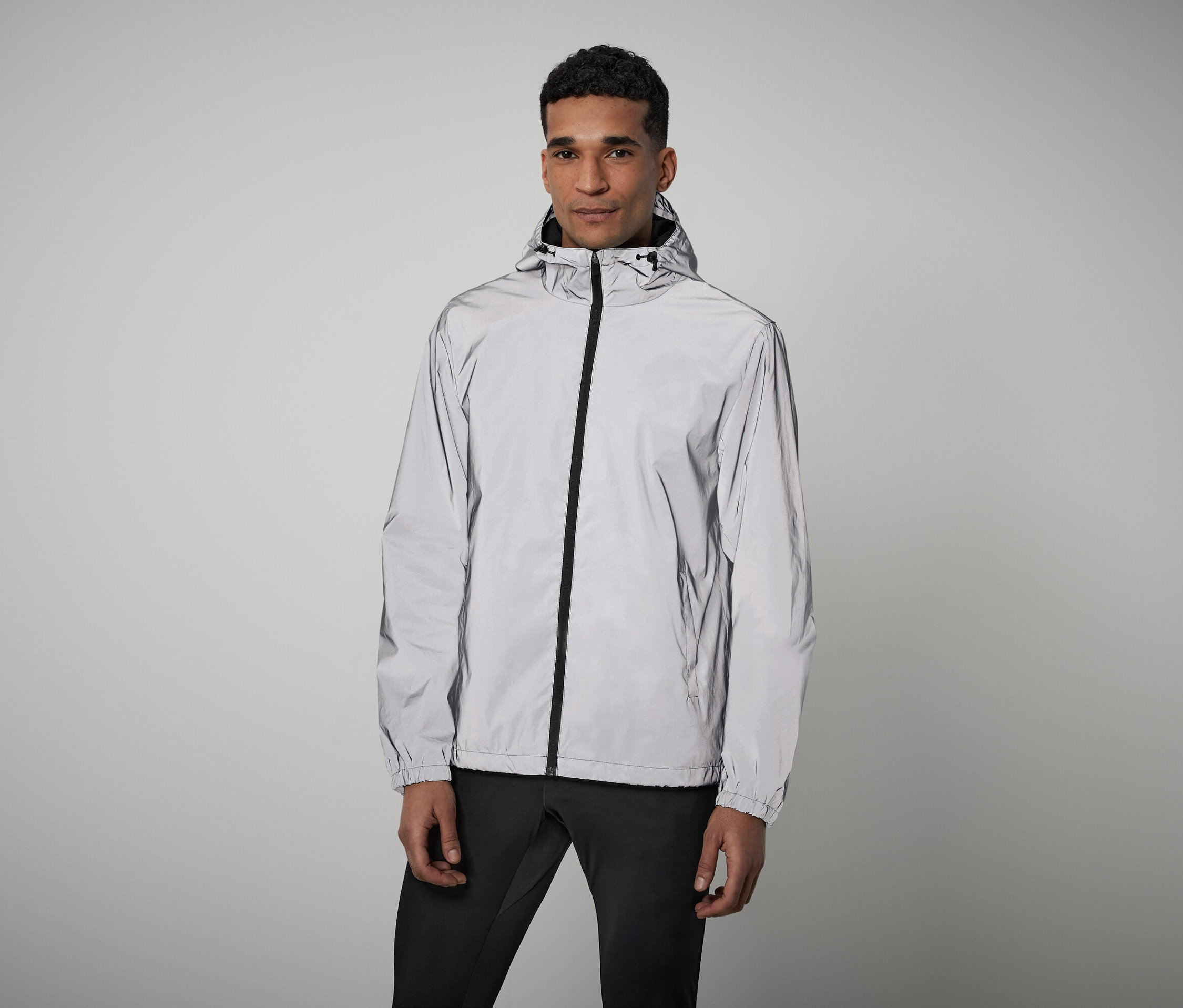 Un homme debout portant une veste grise réfléchissante à fermeture éclair avec capuche et un pantalon noir.