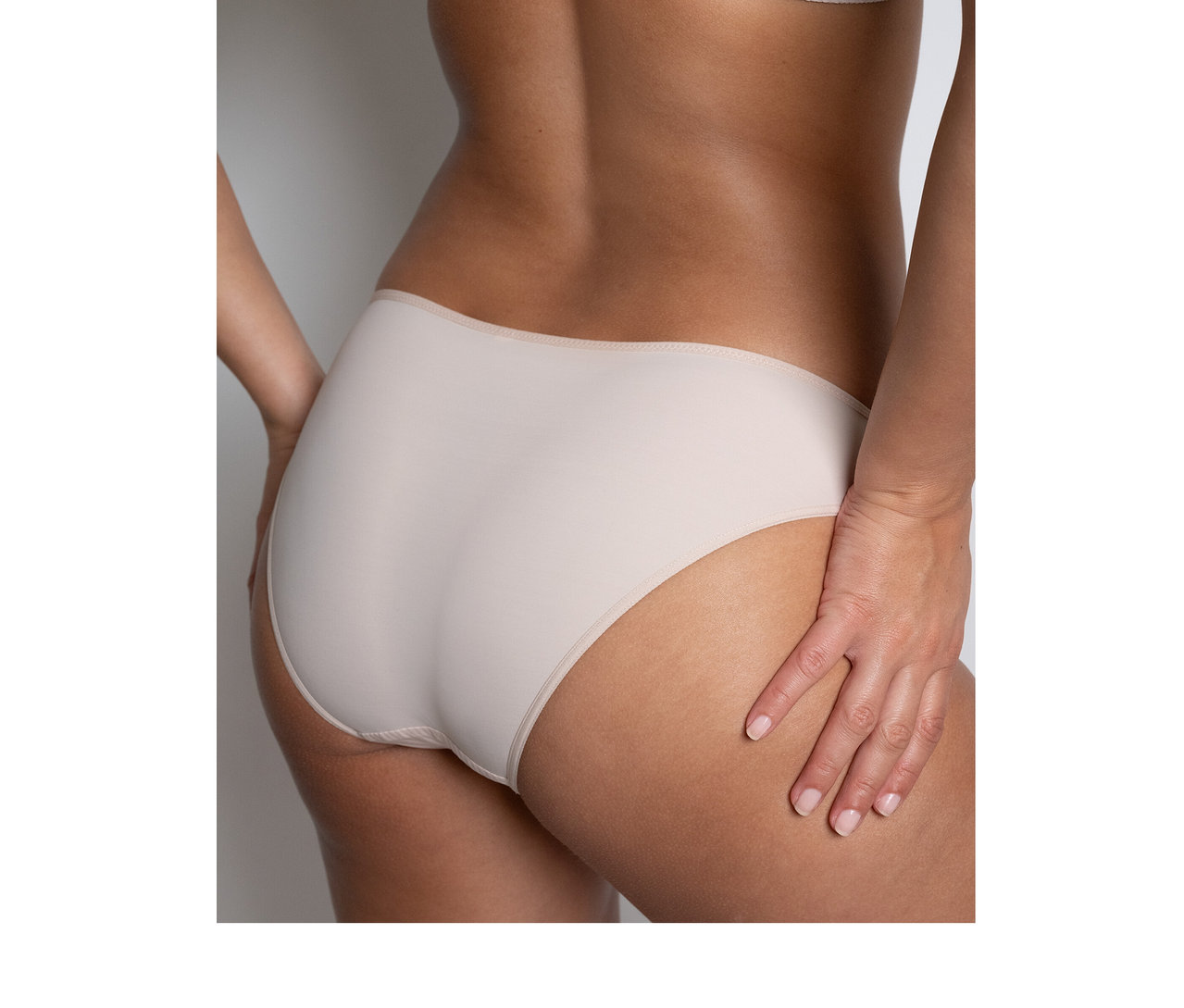 Femme de dos portant un slip « Nais » Passionata couleur dune et un soutien-gorge assorti.