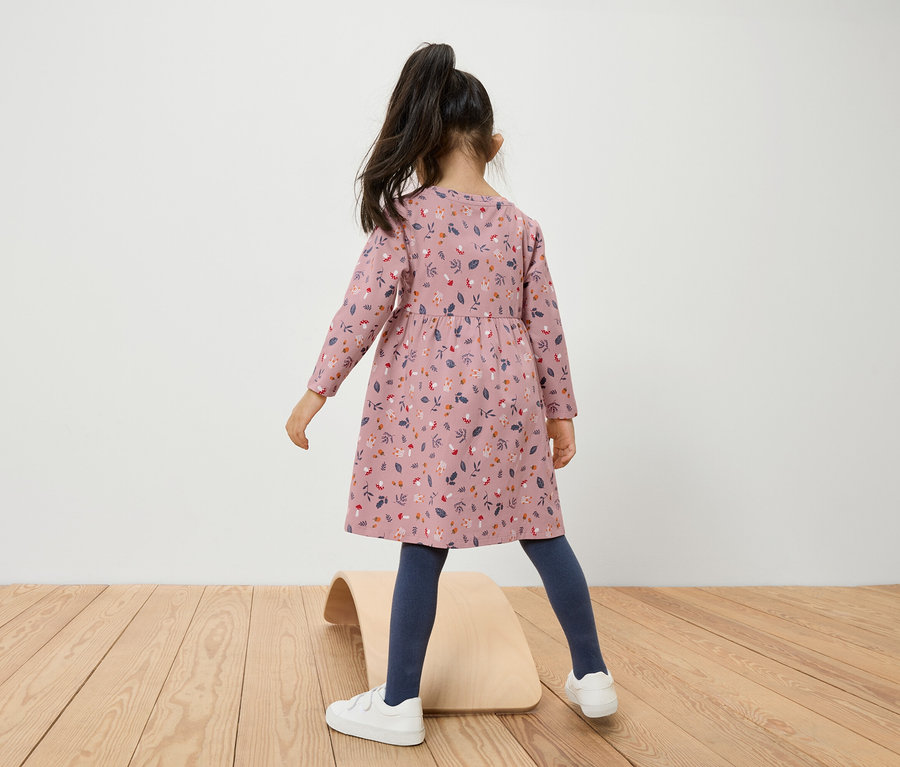 Une fille en robe à fleurs se tient sur une planche d'équilibre en bois.