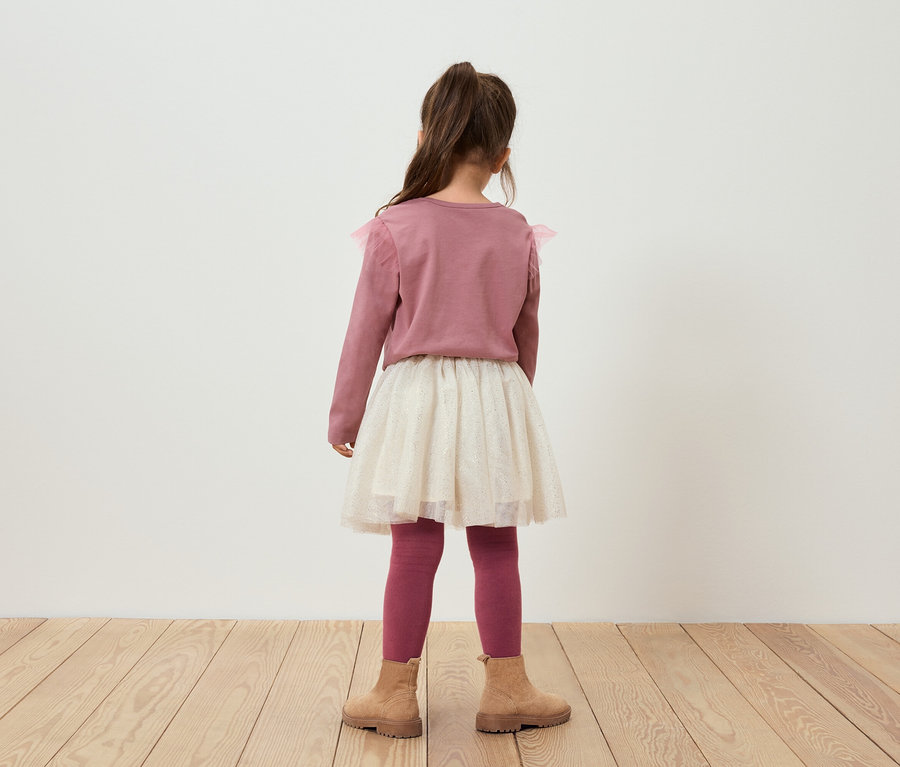 Une fille, dos à la caméra, porte un pull rose, une jupe pailletée, des leggings roses et des bottes marron.