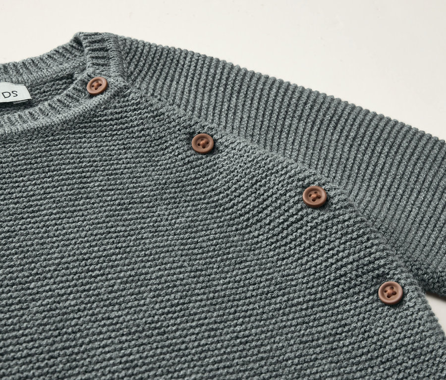 Gros plan d'un ensemble en maille gris pour bébé avec des boutons marron.
