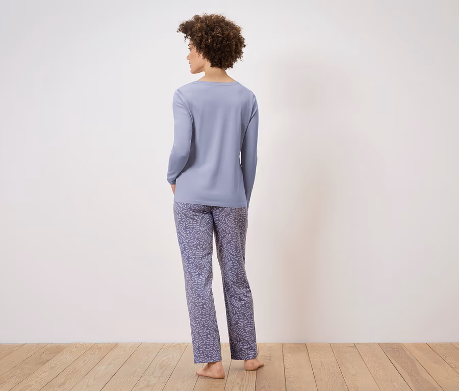 Une femme, vue de dos, porte un pyjama violet clair à manches longues et un pantalon à imprimé feuilles.