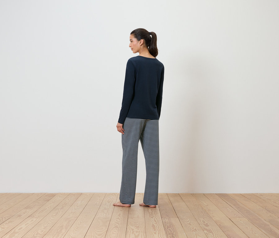 Une femme en pull bleu marine et pantalon rayé, dos à la caméra.