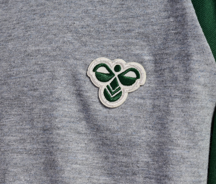 Gros plan sur un t-shirt gris avec des manches raglan vertes et un logo Hummel.