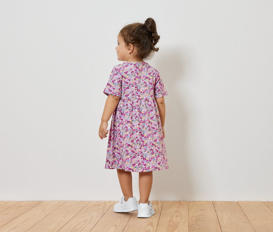 Une petite fille en robe à fleurs et baskets blanches, dos à la caméra.