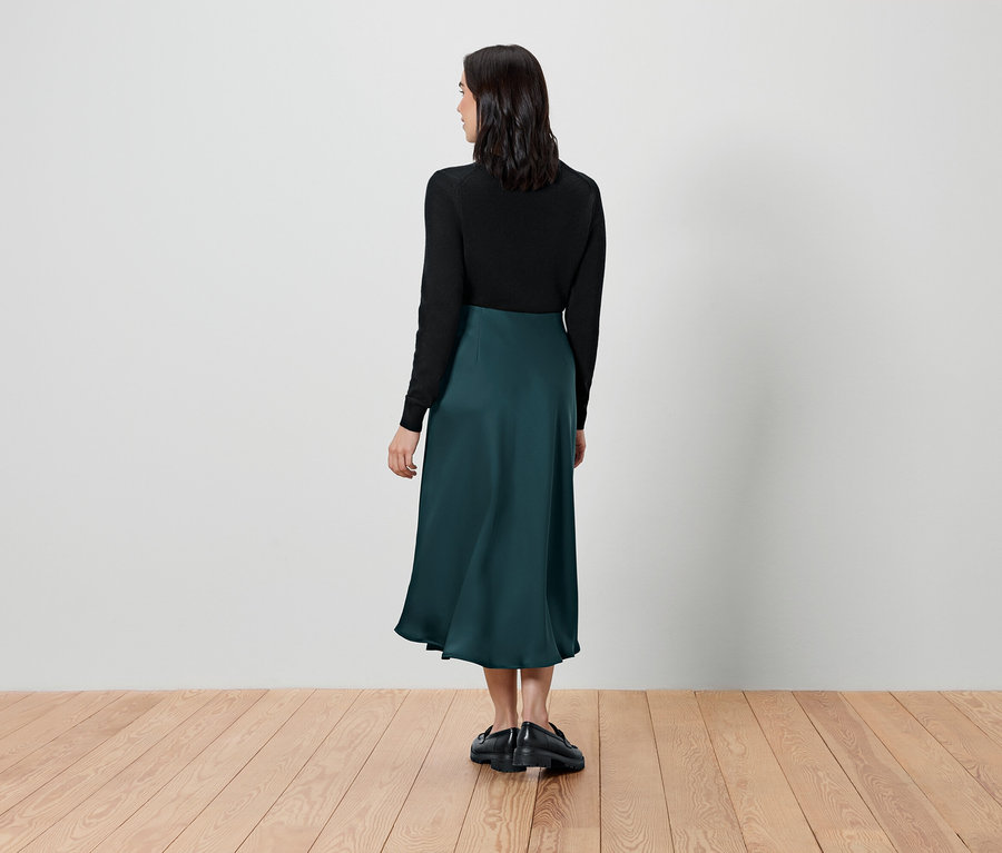 Une femme, vue de dos, porte un haut noir et une jupe verte.