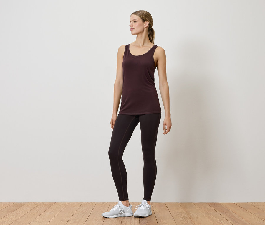 Femme en débardeur et leggings posant en intérieur.