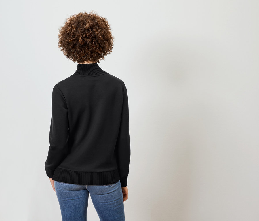 Vue de dos d'une femme aux cheveux bouclés portant un col roulé noir et un jean bleu.