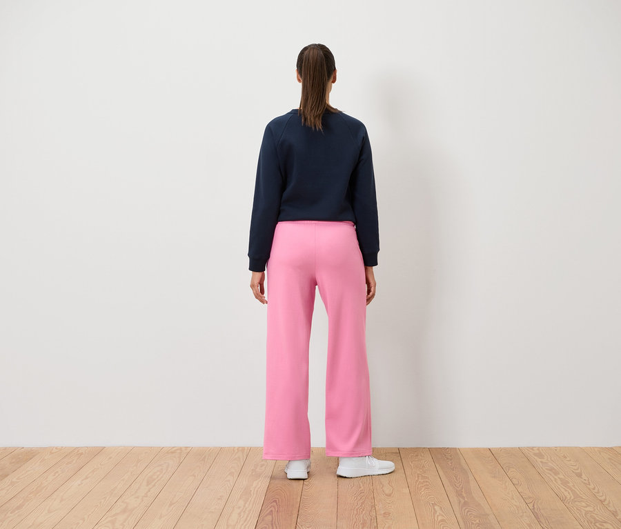 Une femme se tient dos à la caméra portant un sweat-shirt bleu marine et un pantalon rose.