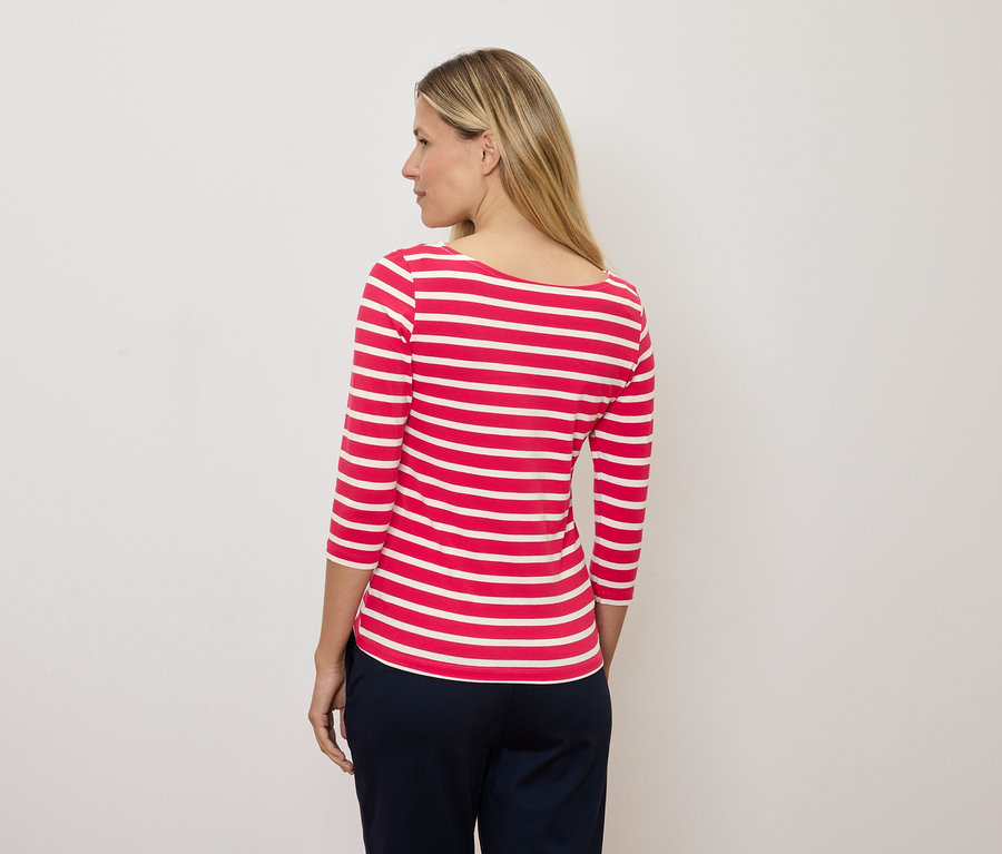 Une femme blonde regarde vers la gauche et porte un t-shirt rayé rouge et blanc à manches trois-quarts.