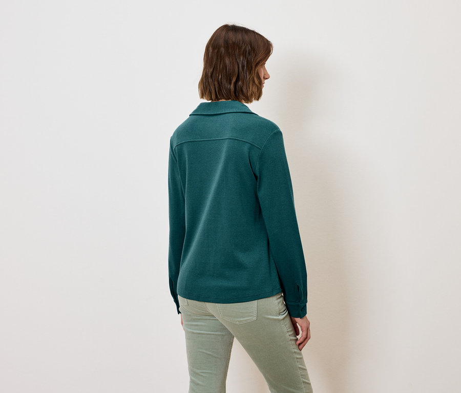 Une femme, vue de dos, porte une chemise à manches longues verte et un pantalon vert.