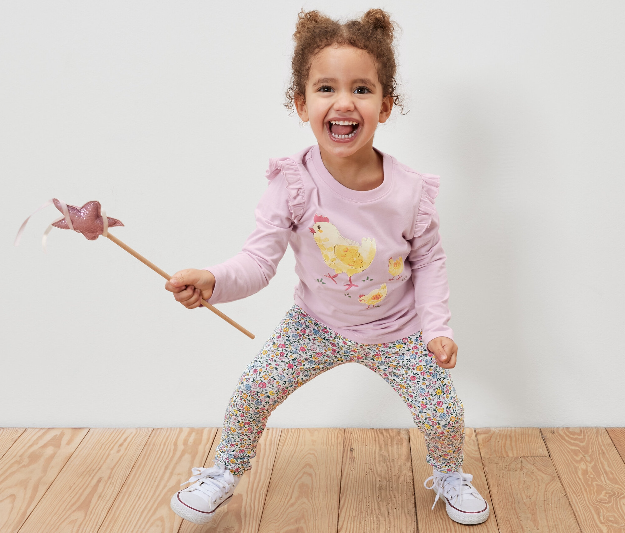 Fillette souriante tenant une baguette magique et portant un 2	Leggings pour enfant, rose et un t-shirt imprimé poulet.