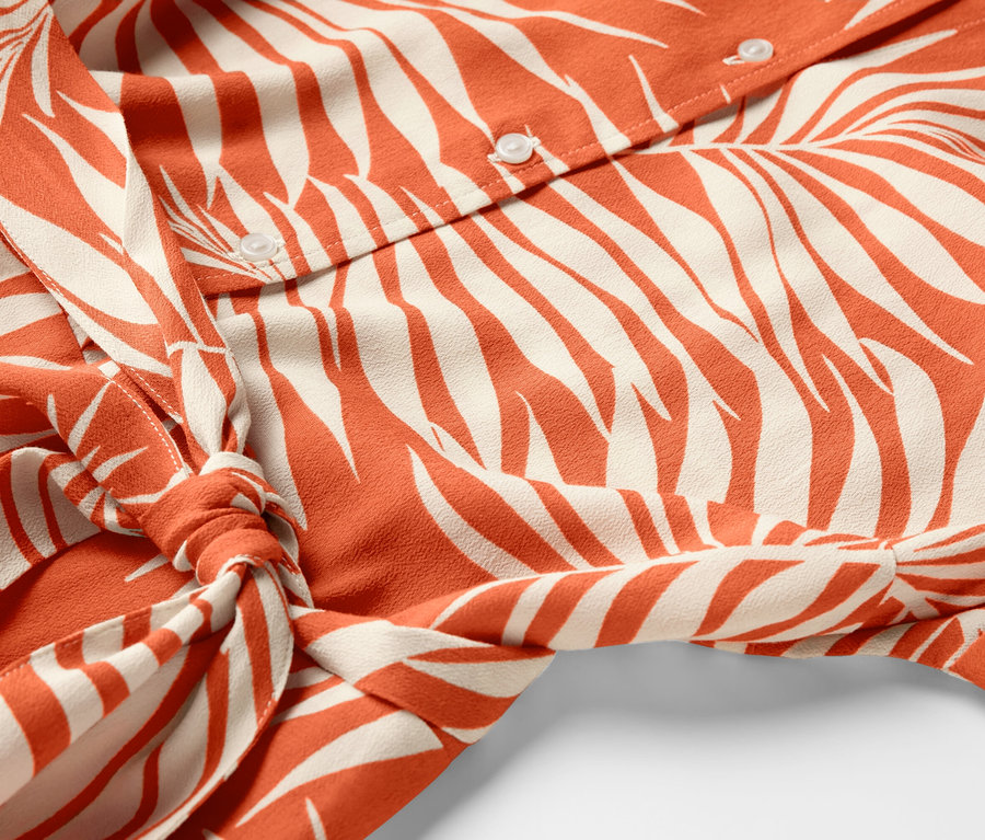 Détail d'une robe chemise imprimée avec boutons et nouée à la taille.